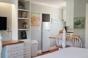 Een praktische keuken met witte kasten, een koelkast, een fornuis, en een eethoek met een stoel en tafel.