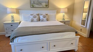 Un dormitorio con una cama, dos mesitas de noche, un cuadro, un espejo y suelo de baldosas.