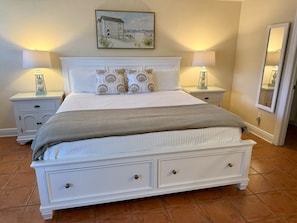 Un dormitorio con una cama, dos mesitas de noche, un cuadro, un espejo y suelo de baldosas.