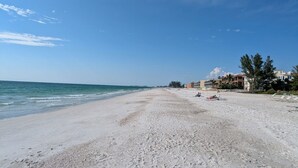 Una playa con cielo despejado, orilla arenosa y edificios al fondo.