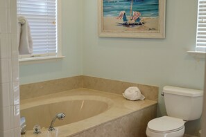A bathroom with a bathtub, toilet, and a painting of a beach scene.