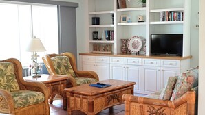 Una sala de estar con muebles de mimbre, un televisor de pantalla plana y una estantería.