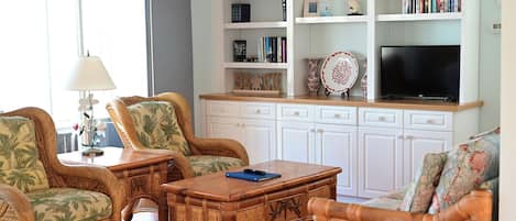 Una sala de estar con muebles de mimbre, un televisor de pantalla plana y una estantería.