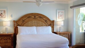 Un dormitorio con una cama grande, dos mesitas de noche, un ventilador de techo y cuadros en las paredes.