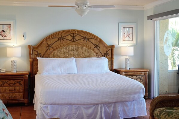 A bedroom with a large bed, two bedside tables, a ceiling fan, and framed artwork on the walls.