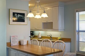 Une cuisine avec des armoires blanches, un plan de travail en bois, un luminaire suspendu et un tableau encadré au mur.
