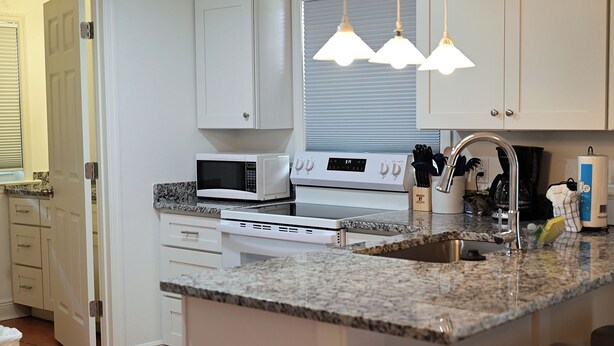 A kitchen with white cabinets, a microwave, an oven, a sink, and pendant lights.