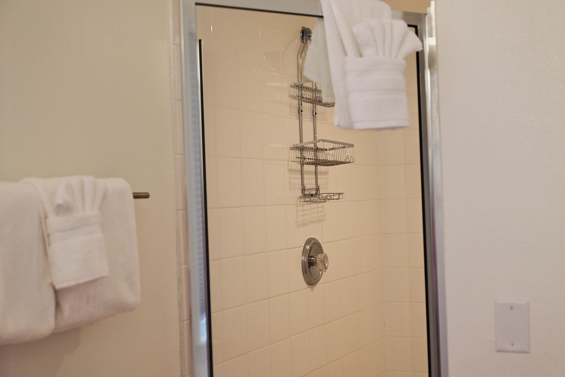 A glass-enclosed shower with a metal rack and a control knob.