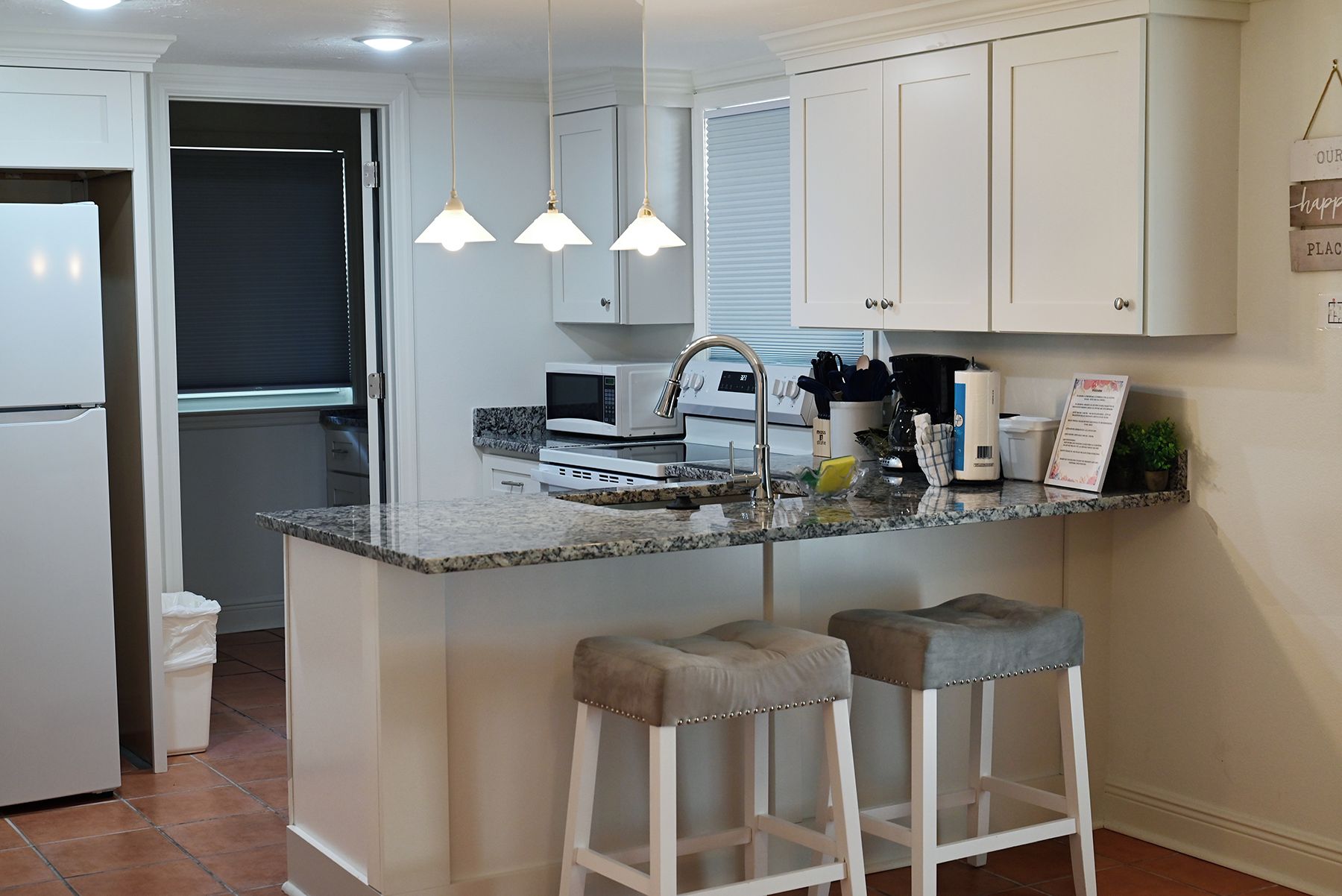 A kitchen with white cabinets, a granite countertop, a built-in microwave, a sink, and two bar stools.