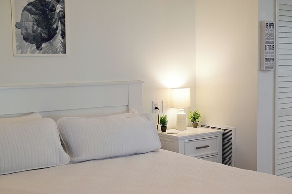 A neatly made bed with a headboard, a bedside table with a lamp, and a wall with a motivational quote.