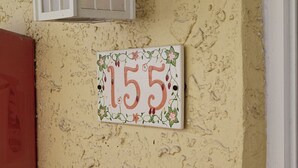 A house number plaque with floral design on a textured wall.