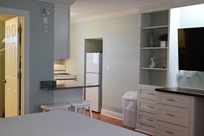 Cocina compacta con refrigerador, estufa y armarios blancos.