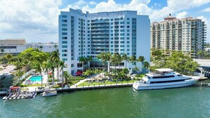 A high-rise hotel with multiple balconies, a pool area, and a yacht docked nearby.