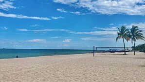 A beach with a volleyball net, palm trees, and a clear sky.
