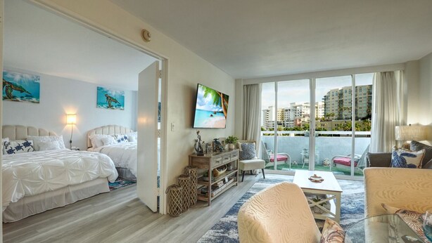 A modern hotel room with a balcony, a bed, a TV, and a seating area with a view of the city.