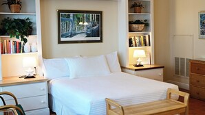 Un dormitorio ordenado con cama, mesitas de noche con lámparas, una estantería y un cuadro en la pared.