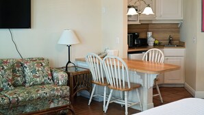 A compact living space with a sofa, a dining table with chairs, a lamp, and a kitchenette. - Cozy Gulf-View Studio Steps from the Beach (Bradenton Beach)
