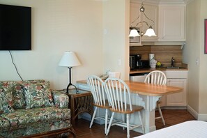 A compact living space with a sofa, a dining table with chairs, a lamp, and a kitchenette. - Cozy Gulf-View Studio Steps from the Beach (Bradenton Beach)