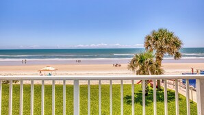 A beach view with a white railing, palm trees, and a clear sky.