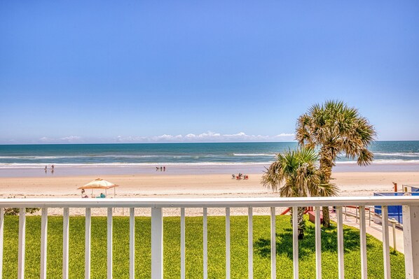 A beach view with a white railing, palm trees, and a clear sky.