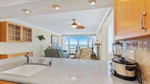 A kitchen with a granite countertop, a sink, wooden cabinets, a ceiling fan, and a view to the outside.