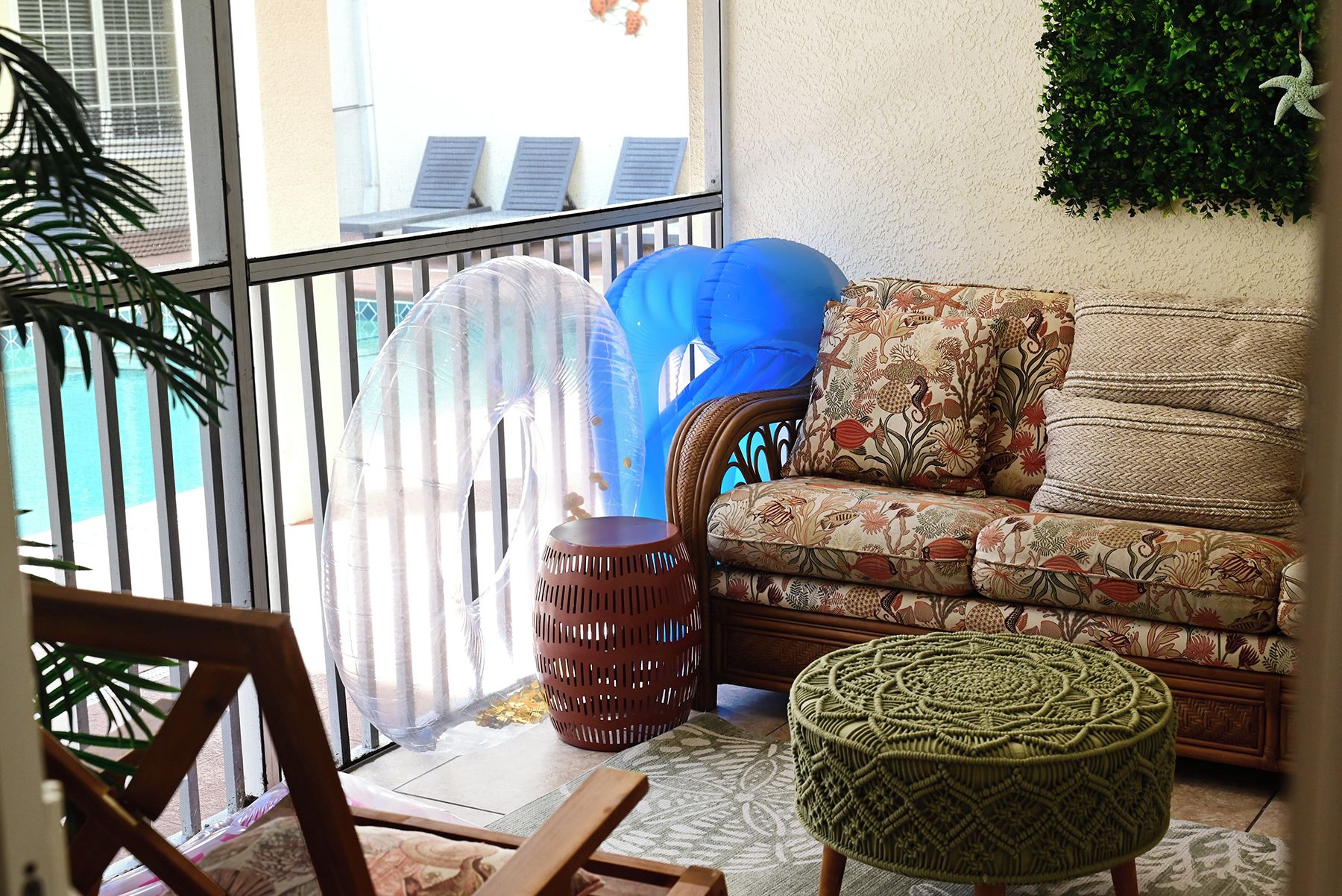 Un balcón con una silla de mimbre, un sofá estampado y un otomano tejido.