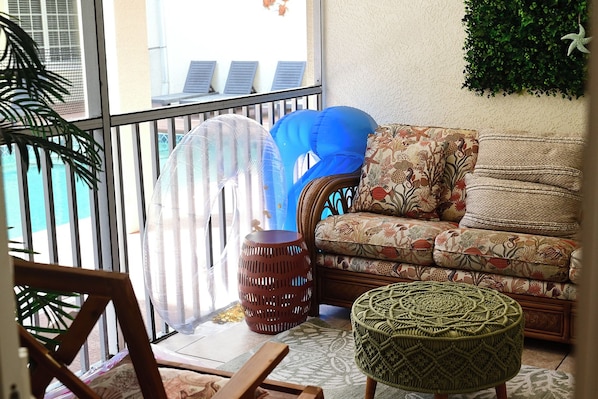 A balcony with a wicker chair, a patterned sofa, and a woven ottoman.