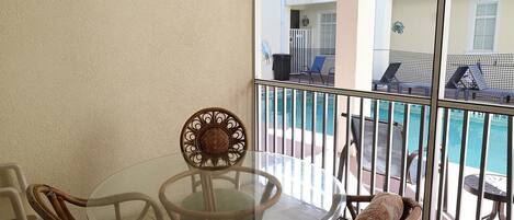 Mesa de vidro com cadeiras de vime numa varanda com vista para a piscina.