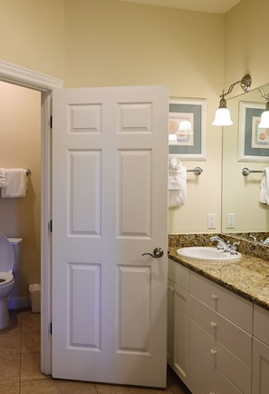 A bathroom with a white door, a toilet, a sink, and a mirror with a light fixture.