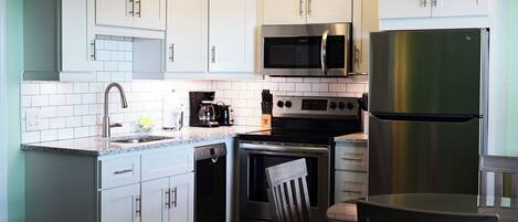 A modern kitchen with white cabinets, a stainless steel refrigerator, a microwave, a coffee maker, and a dishwasher.
