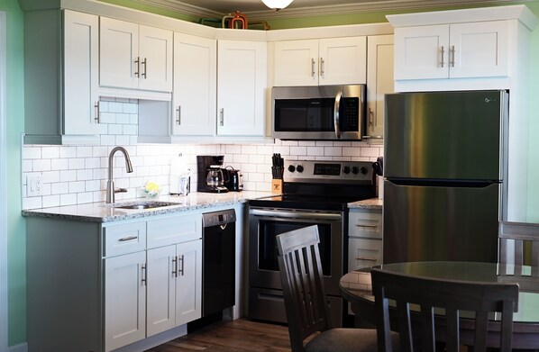 A modern kitchen with white cabinets, a stainless steel refrigerator, a microwave, a coffee maker, and a dishwasher.