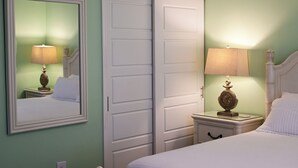 A bedroom with a bed, a nightstand with a lamp, a dresser, and a closet with a mirror. - Waterfront Views · One-Bedroom Bayfront Escape (Bradenton Beach)