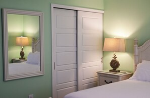 Un dormitorio con cama, mesita de noche con lámpara, cómoda y armario con espejo.