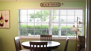 A dining area with a round table and chairs, a sign reading 'BEACH HOUSE', and a window with blinds and starfish decorations. - Waterfront Views · One-Bedroom Bayfront Escape (Bradenton Beach)