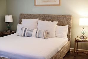 A bed with a woven headboard, white bedding, and decorative pillows. There are two bedside tables with lamps.