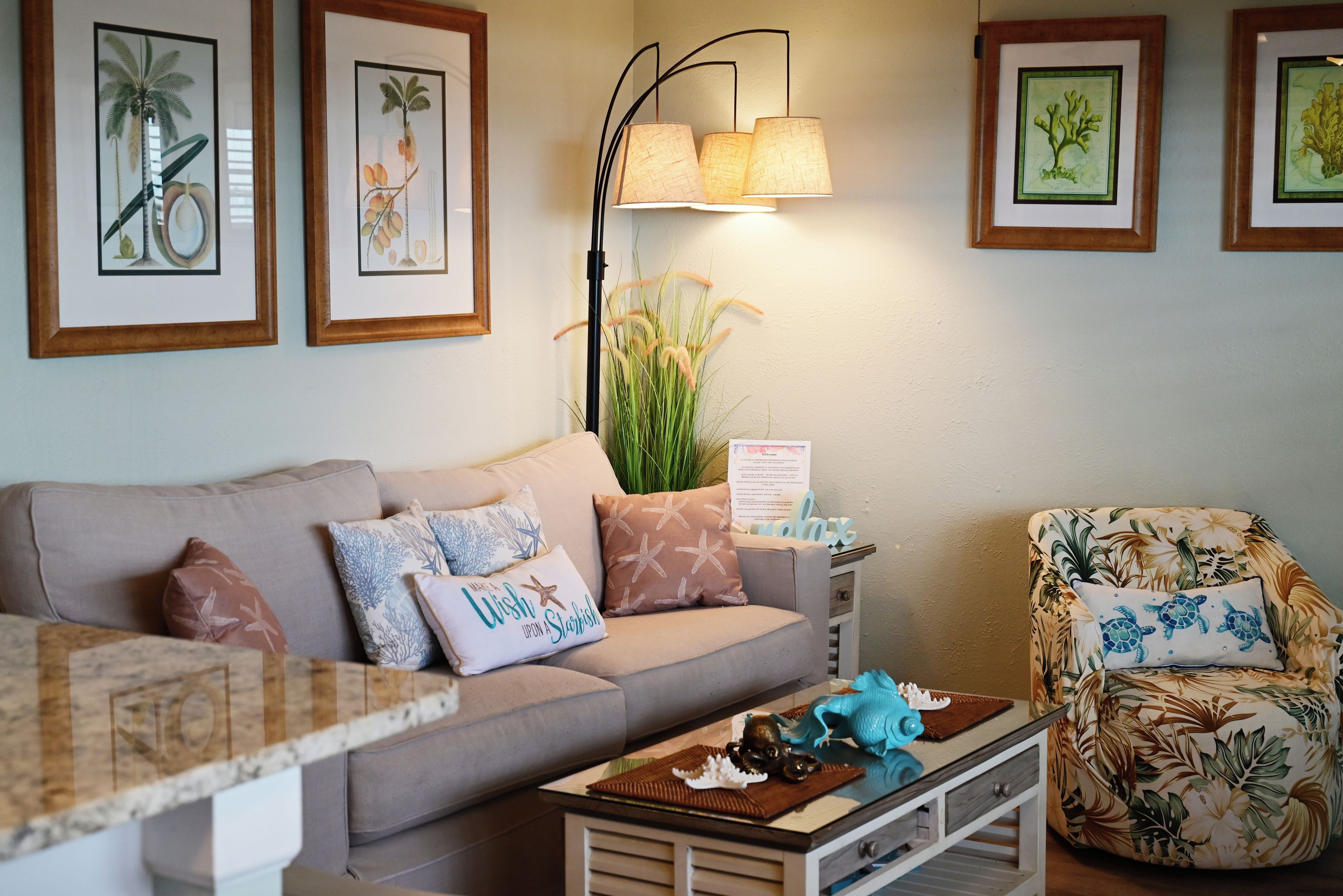 A living room with a sofa, a chair, a coffee table, and framed botanical prints on the wall.