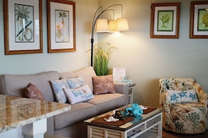 A living room with a sofa, a chair, a coffee table, and framed botanical prints on the wall.