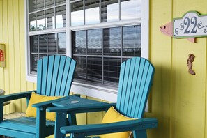 Deux chaises Adirondack bleues avec des coussins jaunes, une fenêtre avec des stores et un panneau indiquant le numéro de la maison, fixé au mur.