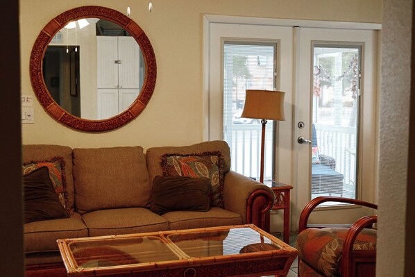 A living room with a sofa, a round mirror, a lamp, and a door with a view outside.