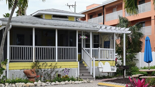 A two-story building with a covered porch, a staircase, and a small garden area with rocks and plants. - Room to Relax · Two-Bedroom Stay on Gulf Drive (Bradenton Beach)
