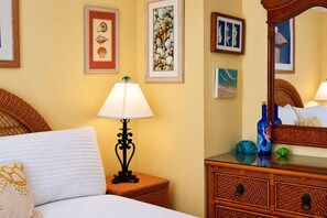 A hotel room with a bed, a nightstand with a lamp, a dresser, and wall art.