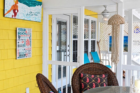 A bright yellow room with a glass door leading to a balcony, wicker furniture, and a wall with a beach-themed poster.
