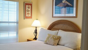 Un lit bien fait, avec une literie blanche, une tête de lit en osier et un seul coussin décoratif.