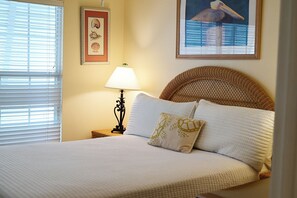 Een opgemaakt bed met witte lakens, een geweven hoofdbord en een decoratief kussen.
