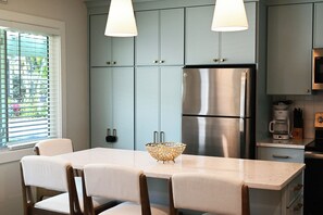 A kitchen with a stainless steel refrigerator, light blue cabinets, a white dining table with chairs, and pendant lights.