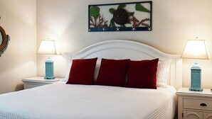Habitación de hotel con cama, dos mesitas de noche con lámparas, un reloj de pared y una obra de arte enmarcada sobre la cama.