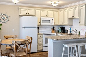 A kitchen with white cabinetry, a refrigerator, a microwave, a stove, and a dining area with a wooden table and chairs. - Relaxed Luxury · Refined North-Side 1 bedroom (Bradenton Beach)
