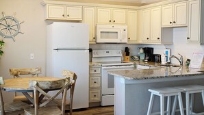 Una cocina con armarios blancos, un refrigerador, un microondas, un horno, un lavamanos y un taburete de bar.