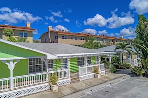 Un edificio residencial con fachada verde, barandillas blancas y un porche cubierto.