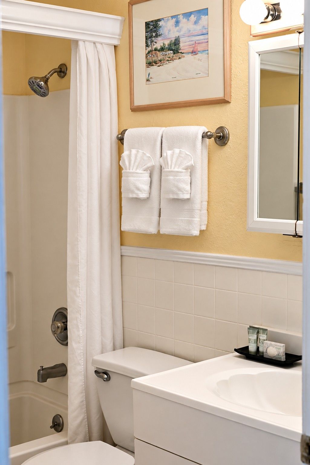 A bathroom with a shower, toilet, sink, and a framed picture on the wall.